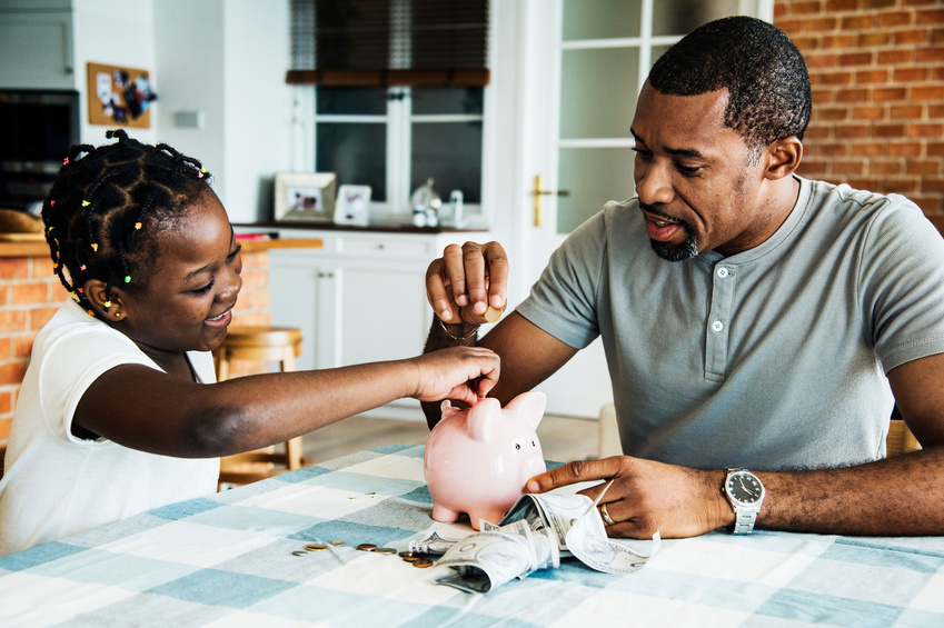 man and school age girl putting coins into pink piggy bank